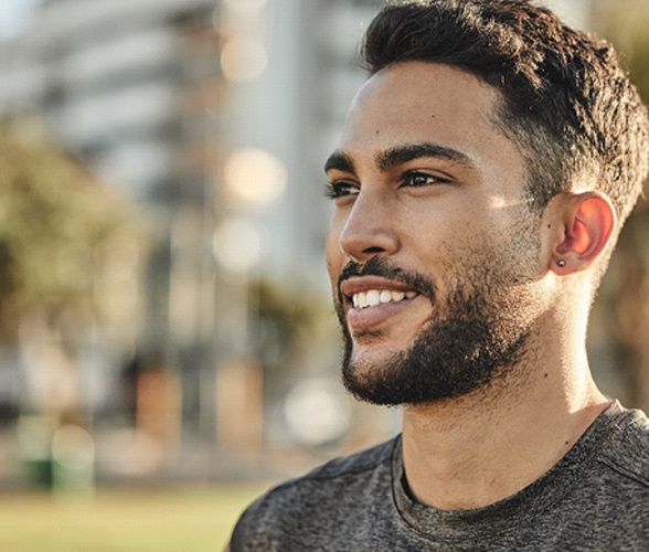 a side profile of a person standing in a park and smiling