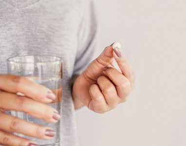 Woman holding a glass of water and pill